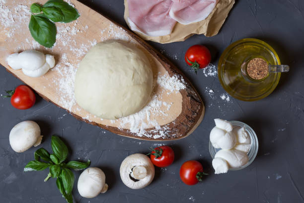 istock Raw dough for pizza with ingredients: mushrooms, tomatoes, ham, mozzarella, oil, basil on table 1159635723