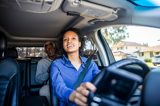 A young black woman drives a passenger in her car as a professional driver.