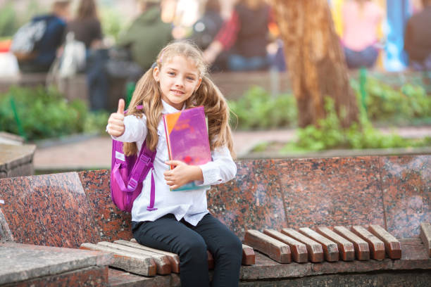 istock Schoolgirl with a backpack and book outdoors. Education and learning concept. 1159638360