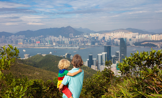 Family with kids hiking in Hong Kong mountains. Beautiful landscape with hills, sea and city skyscrapers in Hong Kong, China. Outdoor activity in the nature for parents and children.
