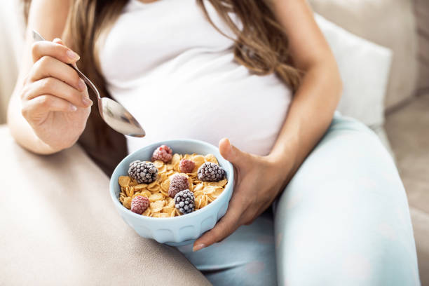 Close up of happy pregnant woman eating cereals with fruits for breakfast in bed at home stock photo