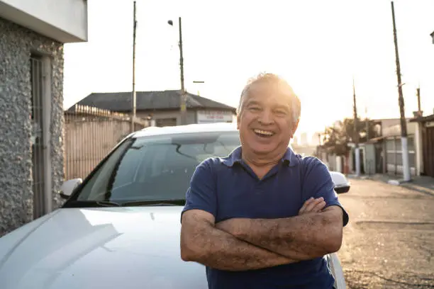 Portrait of smiling senior man in front of a car and looking at camera