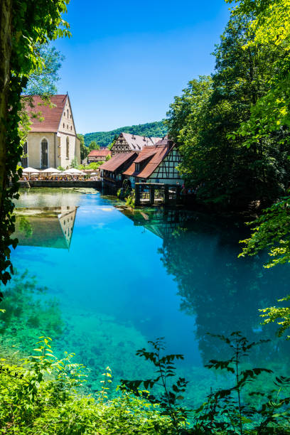 Timbered house water mill and many people mostly tourists reflecting in crystal clear blue water of blue pot (Blautopf) stock photo