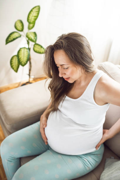 kobieta w ciąży z bólem pleców siedzi na łóżku - backache lumbar vertebra human spine posture zdjęcia i obrazy z banku zdjęć