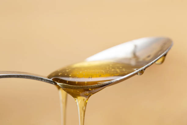 miel doré brillant dégoulinant au loin d'une cuillère argentée avec un fond brun en bois - syrup brown sugar sugar spoon photos et images de collection