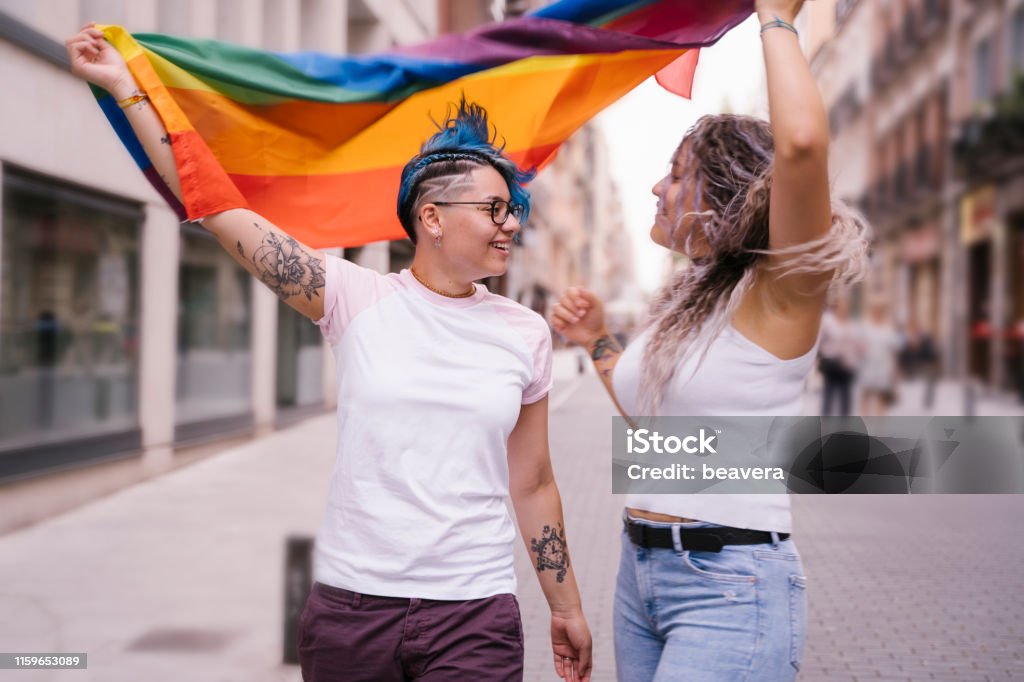 Intimate moment between a lesbian couple. Lesbian couple with playful attitude showing proudly a pride lgbt flag. Lesbian Stock Photo