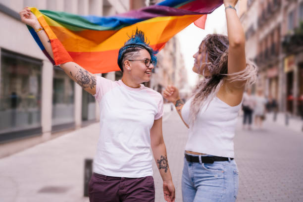 Intimate moment between a lesbian couple. Lesbian couple with playful attitude showing proudly a pride lgbt flag. lesbian pride stock pictures, royalty-free photos & images