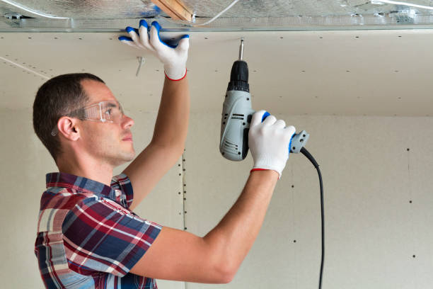 istock Young man in goggles fixing drywall suspended ceiling to metal frame using electrical screwdriver on ceiling insulated with shiny aluminum foil. Renovation, construction, do it yourself concept. 1159657807