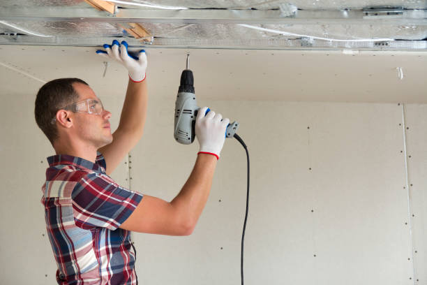 istock Young man in goggles fixing drywall suspended ceiling to metal frame using electrical screwdriver on ceiling insulated with shiny aluminum foil. Renovation, construction, do it yourself concept. 1159657830
