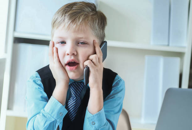 istock Smart little boy in suit working on computer, taking notes and speaking on the phone emotionally. 1159657920