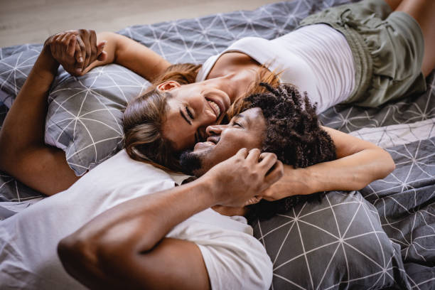 giovane coppia sdraiato letto in camera da letto e sorridente - couple affectionate relaxation high angle view foto e immagini stock