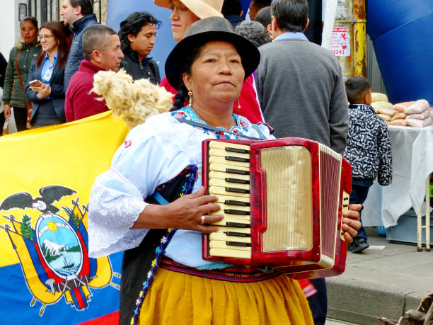 Ecuadorian woman plays on accordion, Ecuador Indigenous village woman dressed as cuencana, typical dress for Azuay province, plays on accordion at the parade on Inti Raymi celebration in Cuenca, Azuay province, Ecuador. Ecuadorian flag at background inti raymi stock pictures, royalty-free photos & images