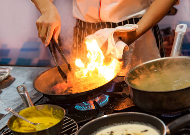 istock Chef cooking with flame in a frying pan on a kitchen stove 1159659100