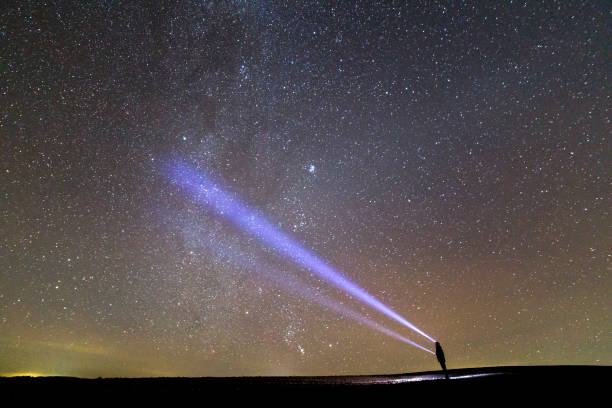 istock Black silhouette of man with head flashlight on grassy field under beautiful dark summer starry sky. 1159660859