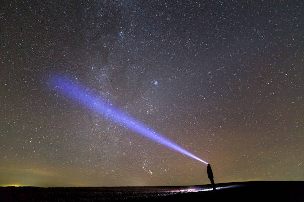 istock Black silhouette of man with head flashlight on grassy field under beautiful dark summer starry sky. 1159660863