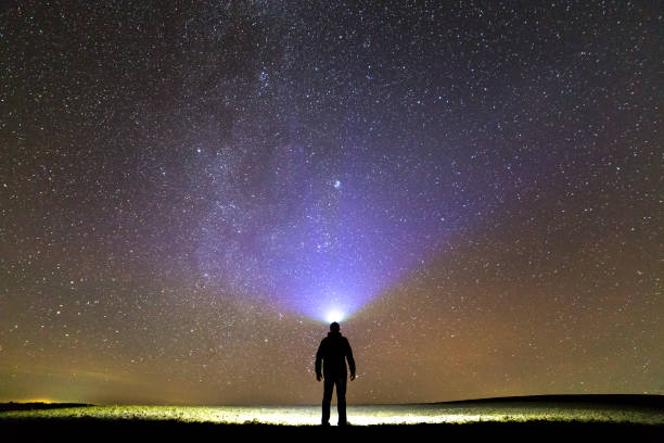 istock Black silhouette of man with head flashlight on grassy field under beautiful dark summer starry sky. 1159660864
