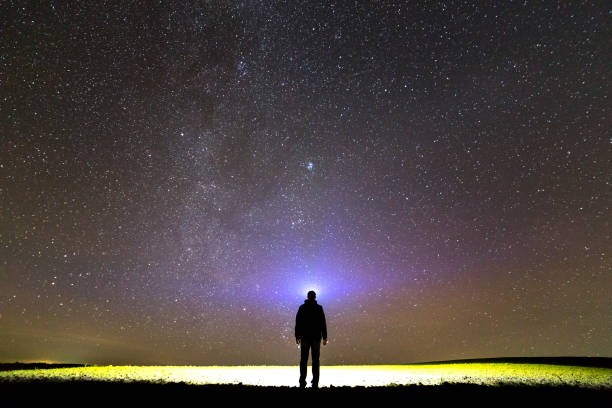 istock Black silhouette of man with head flashlight on grassy field under beautiful dark summer starry sky. 1159661021