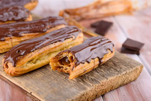 Tasty and beautiful eclairs with chocolate on a wooden board. Appetizing dessert. Party supplies. Flat lay