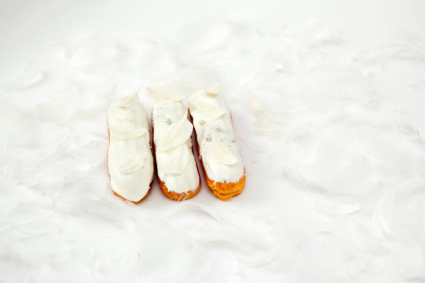 A set of three eclairs with white chocolate decor isolate on a white surface decorated with white feathers