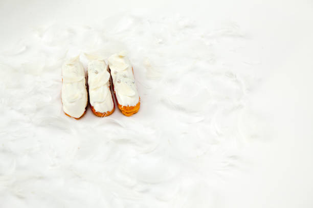 A set of three eclairs with white chocolate decor isolate on a white surface decorated with white feathers