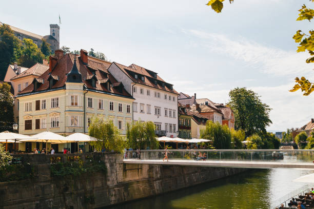 A beautiful view at river Ljubljanica, Cankarjevo Nabrezje, bridges and Ljubljana Castle tower, the tourist centre of Ljubljana, the capital of Slovenia. With people relaxing in cafes at the both banks of the river Ljubljana, Slovenia - September, 8 2018: A beautiful view at river Ljubljanica, Cankarjevo Nabrezje, bridges and Ljubljana Castle tower, the tourist centre of Ljubljana, the capital of Slovenia. With people relaxing in cafes at the both banks of the river ljubljana castle stock pictures, royalty-free photos & images