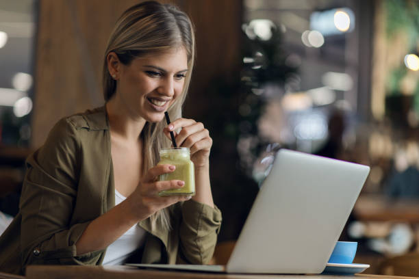 istock Smiling woman drinking smoothie and and reading something from laptop 1159665855