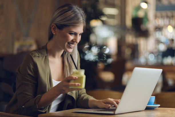 istock Smiling woman drinking smoothie and and reading something from laptop 1159665972