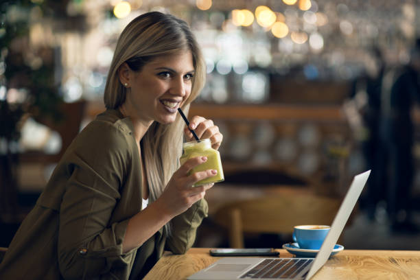 istock Smiling woman drinking smoothie while working in a cafe 1159666071