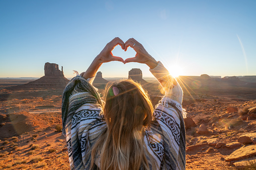 Woman loves USA, makes heart shape finger frame; Rear view of woman on rock at Monument Valley in USA. People travel America concept