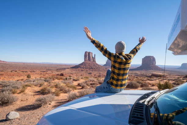 Young man with rental motor home enjoying road trip in USA Road trip concept; Young man outside RV looking at landscape arms outstretched ; national parks and nature ready for adventure monument valley photos stock pictures, royalty-free photos & images