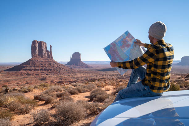 roadtrip-konzept; junger mann außerhalb des autos mit blick auf die roadmap für wegbeschreibungen zur erkundung von nationalparks und natur bereit für abenteuer - navajo national monument stock-fotos und bilder