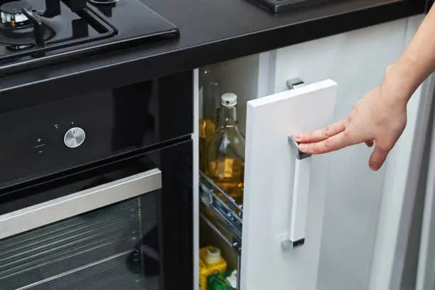 Photo of Woman hand open a kitchen storage cabinet in modern interior