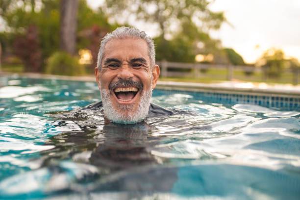 homme aîné riant dans la piscine - active seniors retirement enjoyment swimming pool photos et images de collection