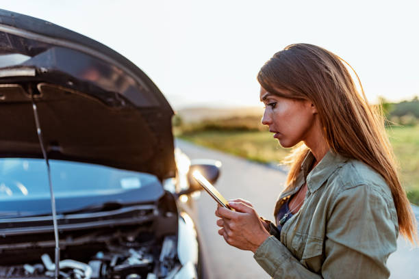 istock Young woman typing text message on mobile phone next to her broken car 1159673558