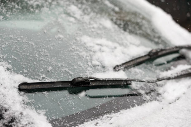 auto-wischer klingen reinigen schnee von autofenstern. schneeflocken bedeckten das auto mit einer dicken schicht. sicheres fahren mit arbeitsfähigen scheibenwischern und sauberer windschutzscheibe. - frozen windshield cold car stock-fotos und bilder