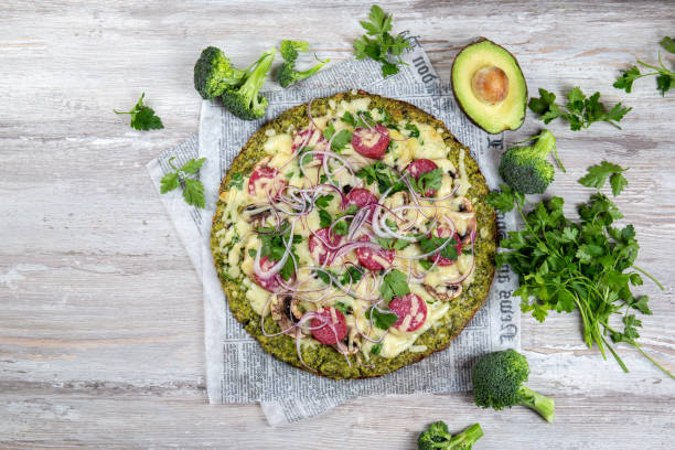 crust broccoli basis low carbs keto pizza mit salami, avocado auf vintage newspapper. ansicht von oben - zucchini vegetable freshness green stock-fotos und bilder
