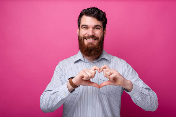 istock Love concept. Young bearded man smiling at the camera making a heart gesture. 1159675854