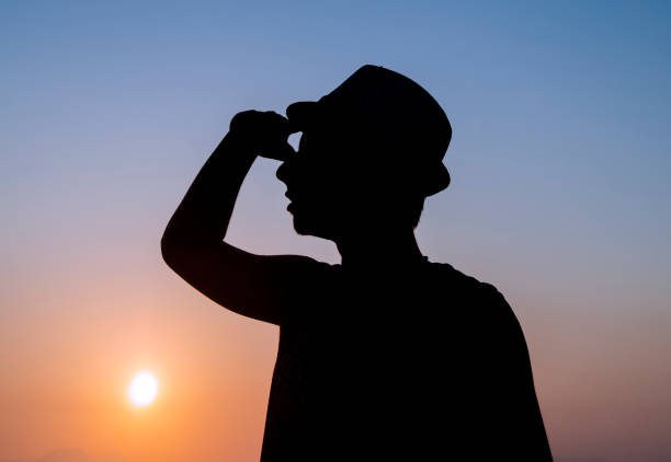 istock Silhouette of young man with hat looking on colorful sunset sky 1159678652