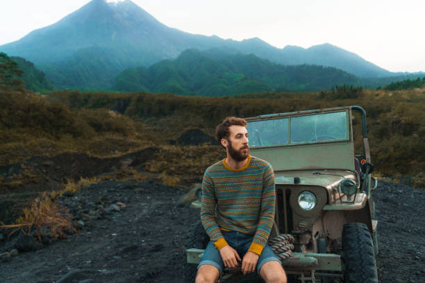 istock Man sitting on old fashioned SUV on the background of Merapi volcano 1159678856