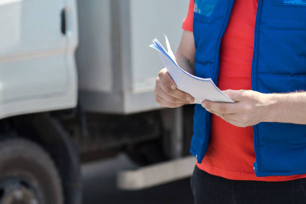 istock Courier driver in uniform making notes in document and delivery white truck behinde him 1159679304