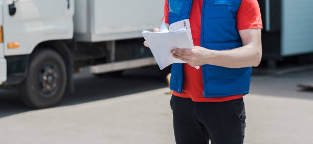 istock Courier driver in uniform making notes in document and delivery white truck behinde him 1159679309