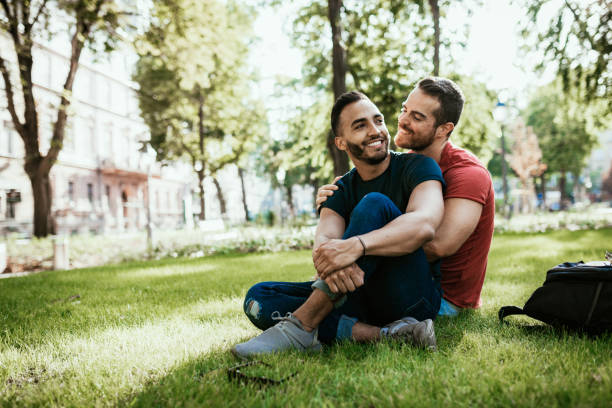 coppia gay - uomini millenari latino ed europei - che si godono nel parco in estate - gay man homosexual couple homosexual men foto e immagini stock