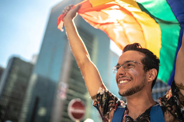Young gay man holding rainbow flag during pride parade Young gay man holding rainbow flag during pride parade lgbtqia pride event photos stock pictures, royalty-free photos & images