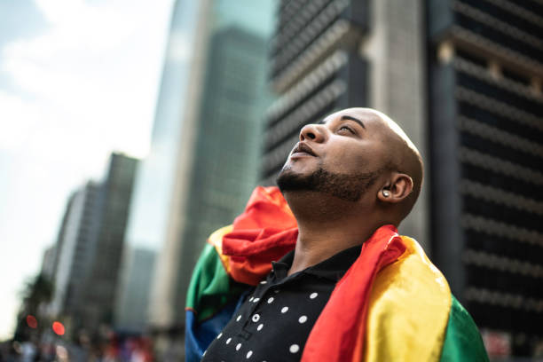 jeune homme gai retenant le drapeau d'arc-en-ciel pendant le défilé de fierté - gay pride flag gay pride gay man homosexual photos et images de collection