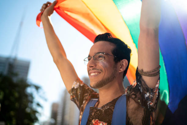 istock Young gay man holding rainbow flag during pride parade 1159690531