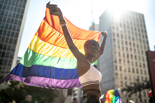 Mujer lesbiana segura sosteniendo la bandera arco iris durante el desfile del orgullo photo