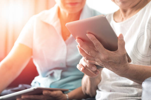 glückliche ältere zwillinge senioren gesellschaft lebensstil mit technologie-konzept. alternde asia-frauen, die tablet und smartphone nutzen, teilen soziale medien gemeinsam im wohlfühl-kreisheim. - 40 weeks stock-fotos und bilder