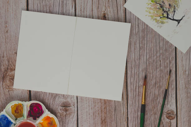 istock Blank watercolor notebook, palette and paintbrushes on wooden background 1159707446