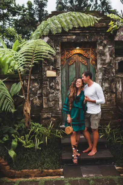 Photo of Happy couple in love smiling and kissing on background of traditional balinese architecture