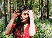 赤いドレスを着た美しい若いブルネットの女性の肖像画は、森林公園で彼女の黒い長い髪に手を持ってカメラに微笑んでいます。魅力的な若い中国のスタイリッシュな女性の屋外ファッショ�